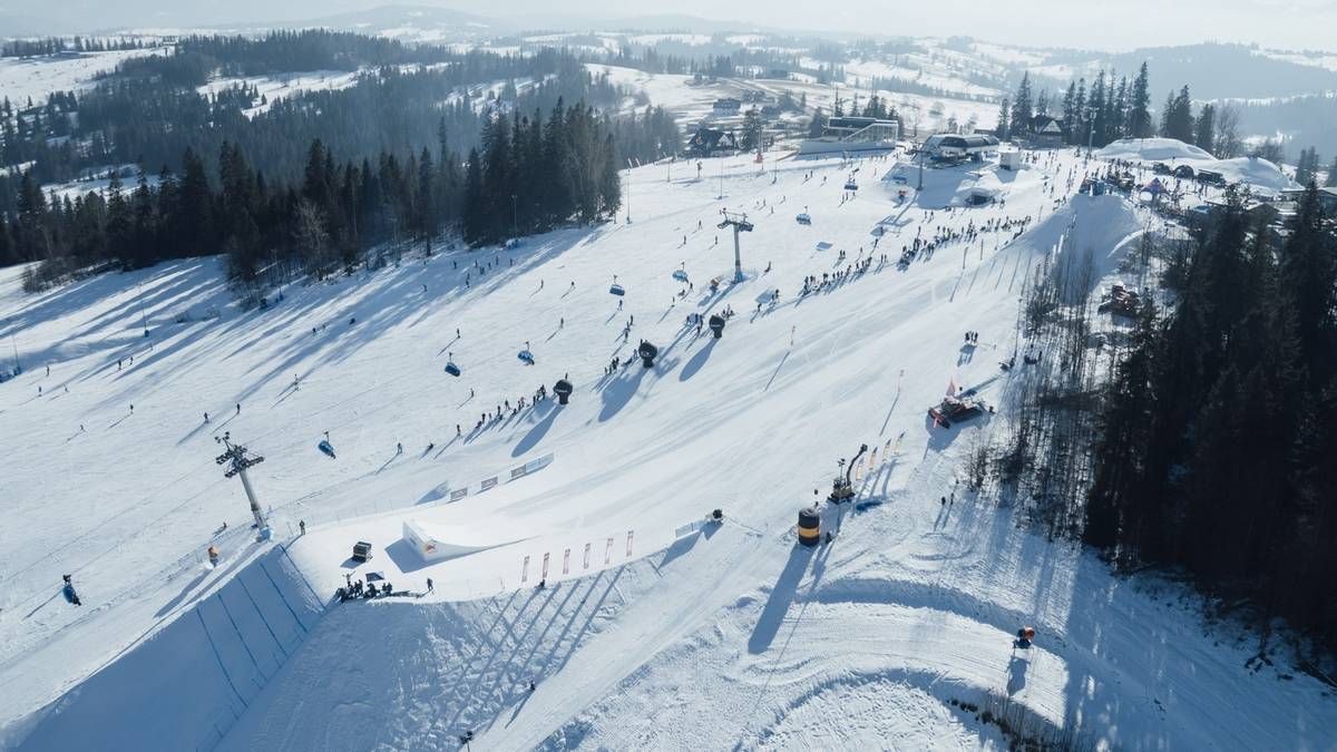 Widok z lotu ptaka na ośnieżony stok narciarski z wytyczonymi trasami i widocznymi narciarzami.