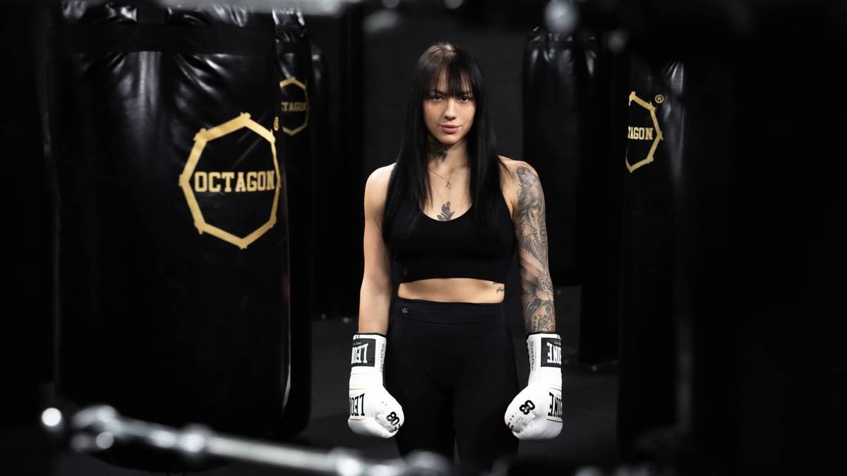 Kobieta w rękawicach bokserskich stoi w sali treningowej.