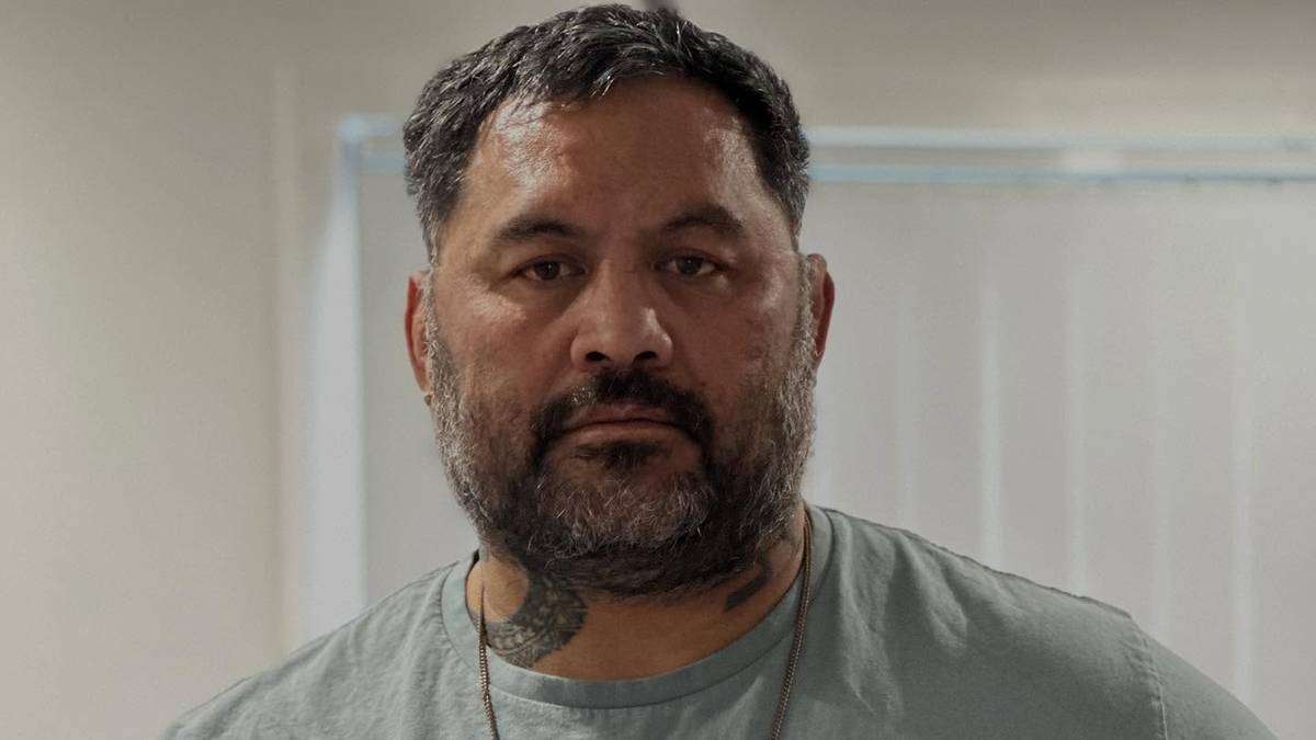 Mężczyzna o ciemnej karnacji, w szarej koszulce, trzyma w ręku dokument.