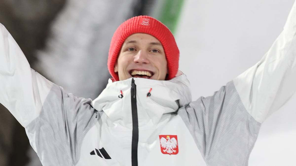 Uśmiechnięta kobieta w białej kurtce narciarskiej z napisem "POLSKA" na piersi, z uniesionymi rękami w geście triumfu.