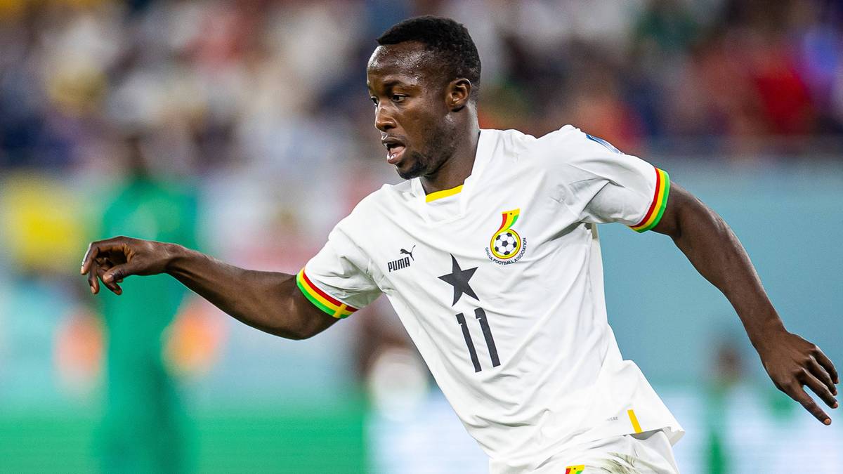 Piłkarz w białej koszulce z numerem 11 drybluje z piłką na boisku.