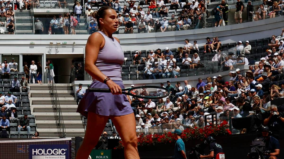 Aryna Sabalenka, tenisistka, podczas meczu, ubrana w strój sportowy, trzyma rakietę tenisową, na tle trybun pełnych kibiców.