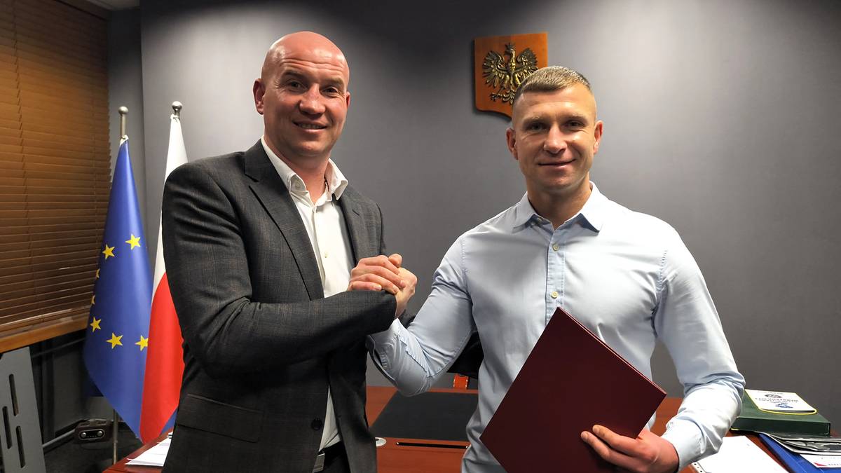 Dw&oacute;ch mężczyzn w garniturach ściska sobie dłonie, jeden z nich trzyma teczkę.