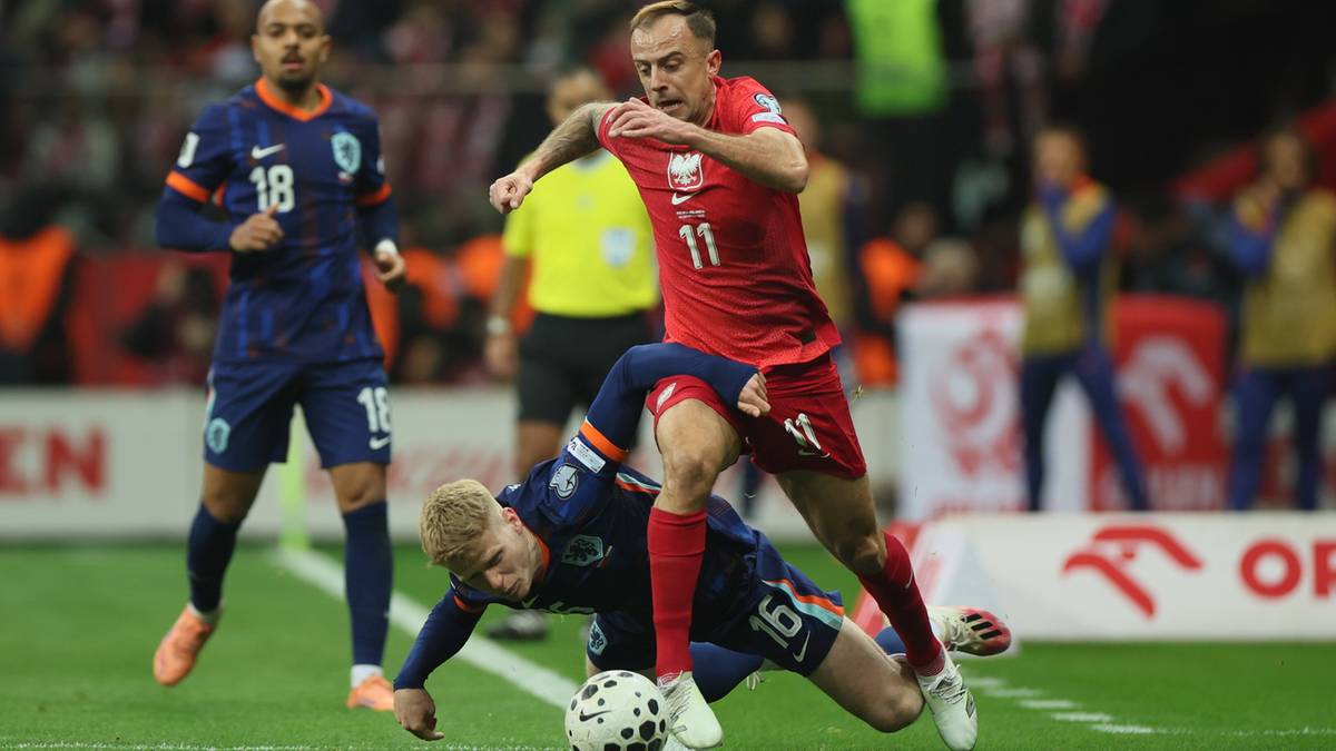 Dwóch piłkarzy walczących o piłkę na boisku, jeden w czerwonej koszulce Polski, drugi w granatowej koszulce Holandii.