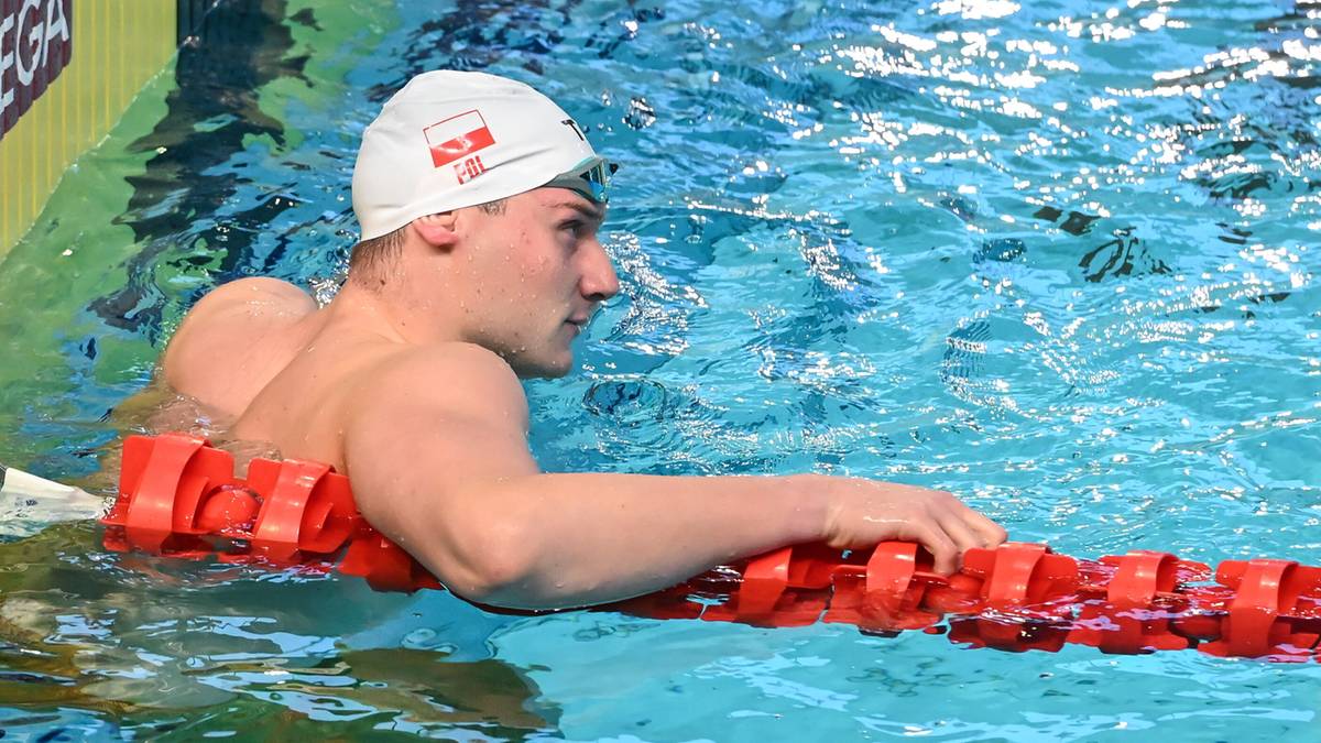 Polski pływak w czepku z biało-czerwoną flagą opiera się o tor pływacki.