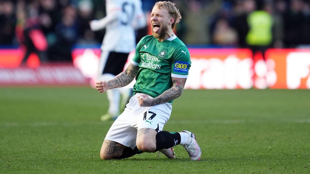 Piłkarz w zielonej koszulce z numerem 17 na boisku, klęczy z zaciśniętą pięścią i wykrzywionymi ustami w geście radości po strzelonej bramce.