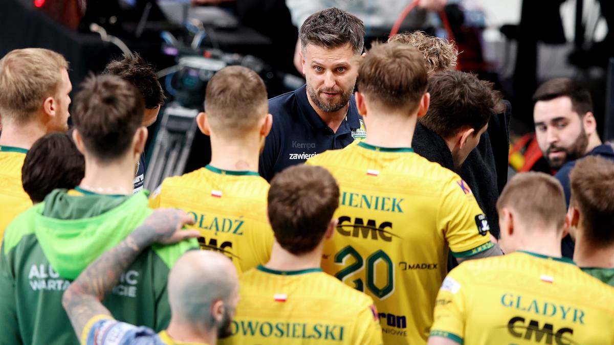 Grupa siatkarzy w żółtych strojach z trenerem w środku, patrzący w tym samym kierunku.