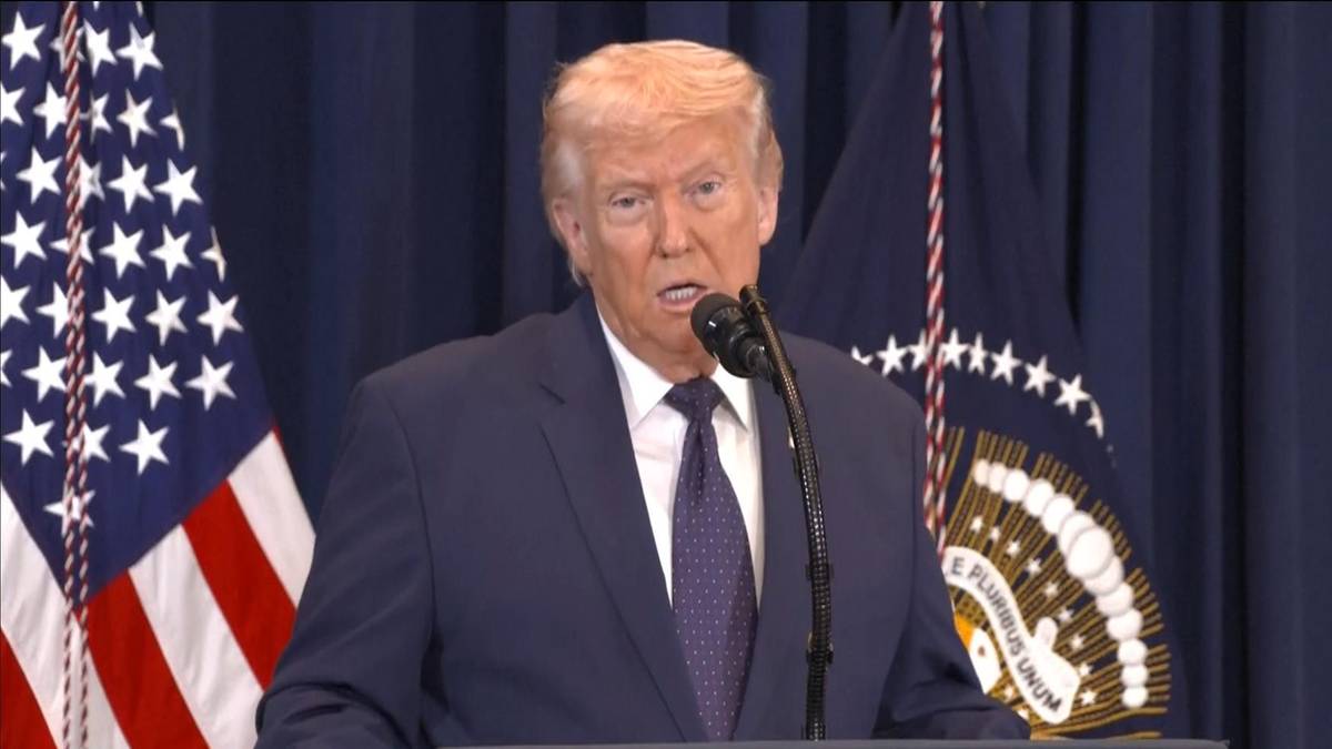 Donald Trump przemawia przy m&oacute;wnicy, za nim amerykańska flaga i flaga z pieczęcią prezydencką.