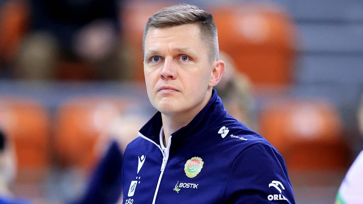 Trener siatkarskiej drużyny BKS w okularach i kurtce sportowej trzyma kartkę z notatkami.