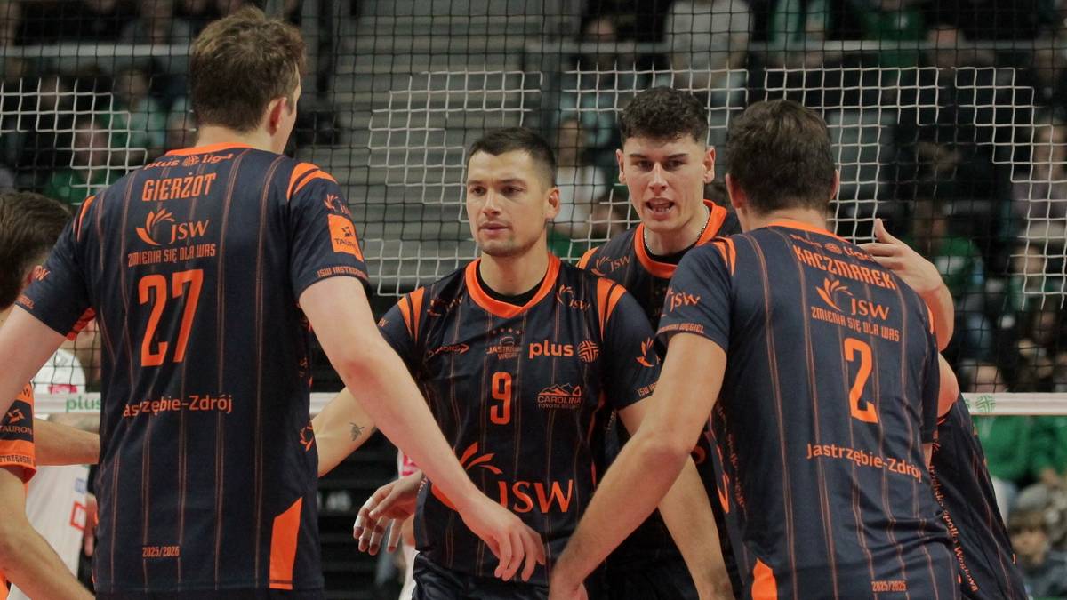 Czterech siatkarzy Jastrzębskiego Węgla w ciemnych strojach z pomarańczowymi detalami, stojących blisko siebie i rozmawiających, prawdopodobnie po wygranym meczu. Na strojach widoczne numery 27, 9 i 2.