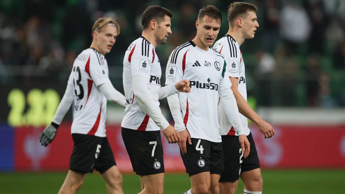 Czterech piłkarzy w białych strojach z czarnymi detalami idzie po boisku.