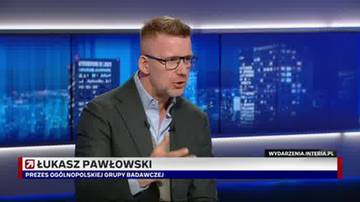 Łukasz Pawłowski, prezes og&oacute;lnopolskiej grupy badawczej, w okularach i ciemnym garniturze, m&oacute;wiący do kamery na tle niebieskiego ekranu z nocnym widokiem miasta.