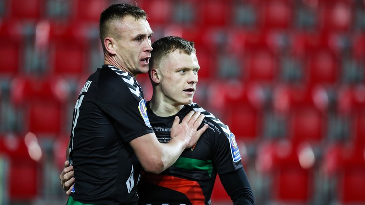 Dw&oacute;ch piłkarzy GKS Tychy, ubranych w czarno-zielone stroje, przytulających się na boisku piłkarskim.