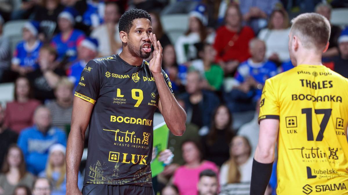 Dwóch siatkarzy w strojach sportowych, jeden w czarnej koszulce z numerem 9, drugi w żółtej koszulce z numerem 17, rozmawia na boisku siatkarskim.