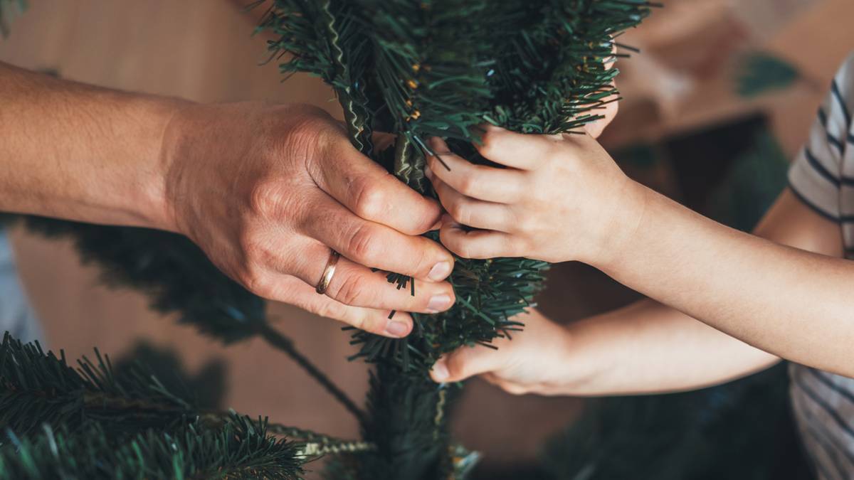 Dłoń dorosłego i dłoń dziecka trzymają się gałęzi sztucznej choinki.