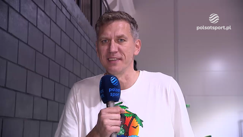 Cezary Trybański, polski koszykarz, trzymający mikrofon z logo Polsat Sport i uśmiechający się do kamery.