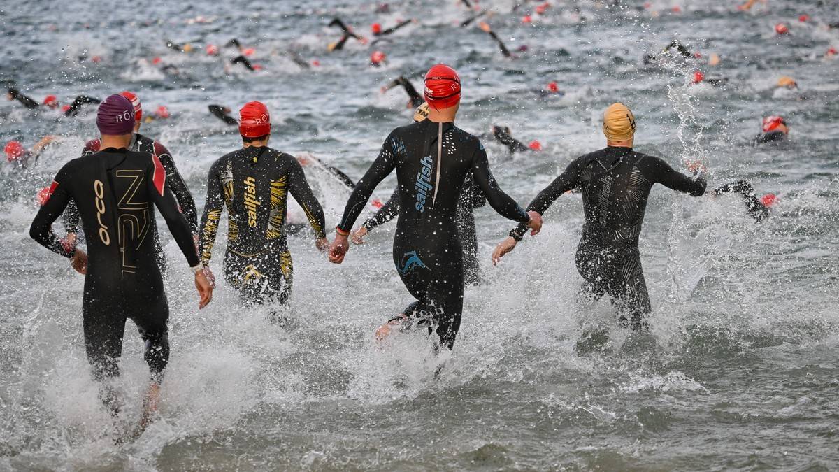 Czterech zawodników w strojach do triathlonu biegnie przez wodę podczas zawodów.