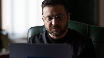 Wołodymyr Zełenski w okularach siedzi przy biurku i patrzy na ekran laptopa.