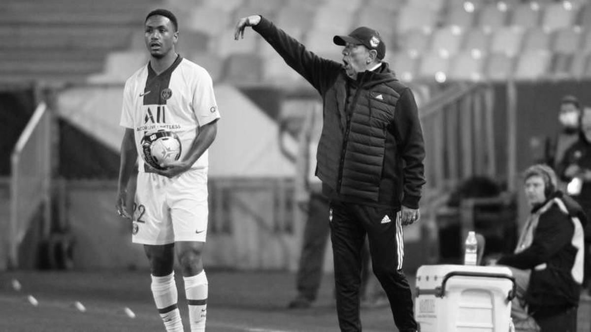 Piłkarz z piłką i trener gestykulujący na boisku.