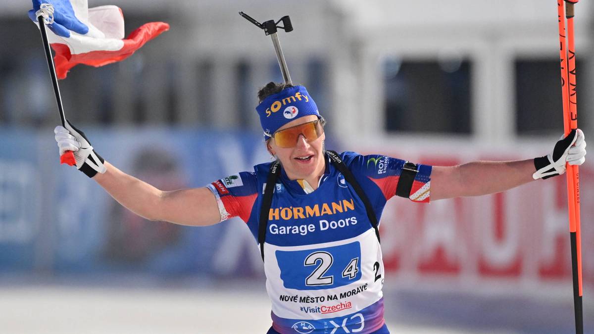 Biathlonistka w okularach przeciwsłonecznych i czapce z flagą Francji radośnie wznosi ręce z radością po zwycięstwie. Na koszulce ma numer 24.