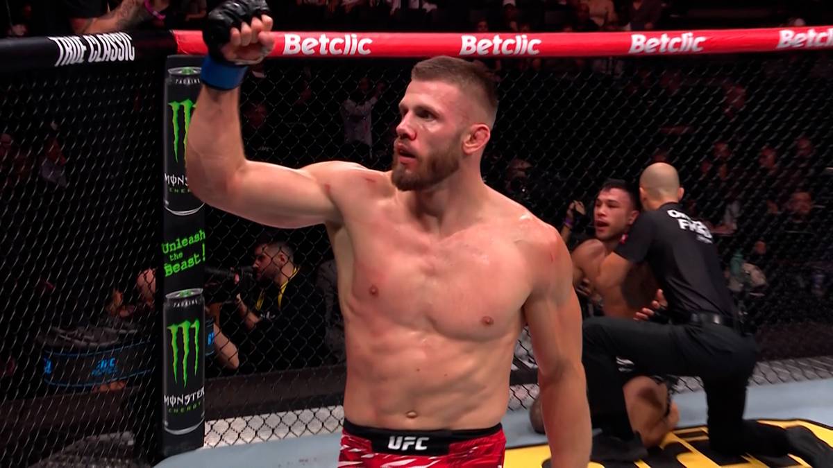 Zawodnik MMA Borys Majchrowski w ringu UFC, uniesiona prawa ręka w geście triumfu, widoczne logo UFC na spodenkach.