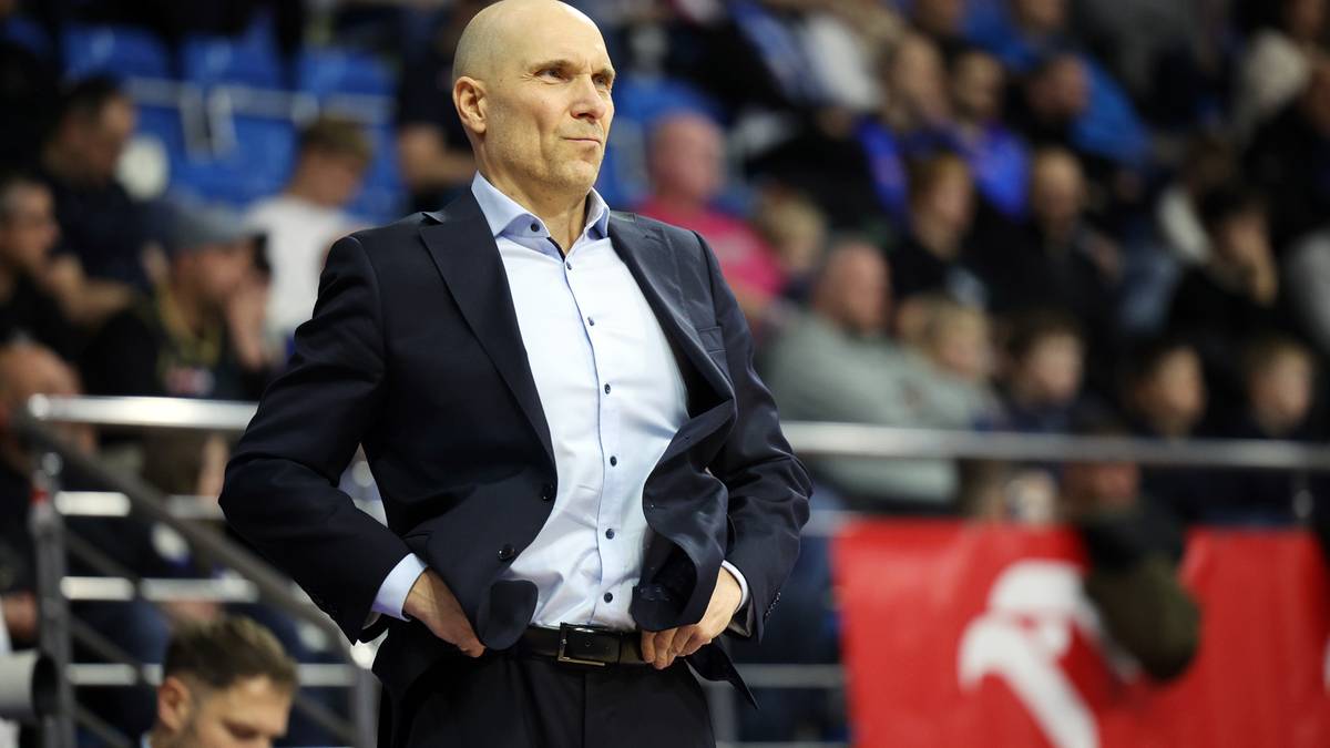 Mężczyzna w garniturze i koszuli stoi na tle trybun.