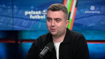 Mężczyzna w czarnej koszuli z kołnierzykiem siedzi przed mikrofonem, na tle ekranu z logiem Polsat Futbol.