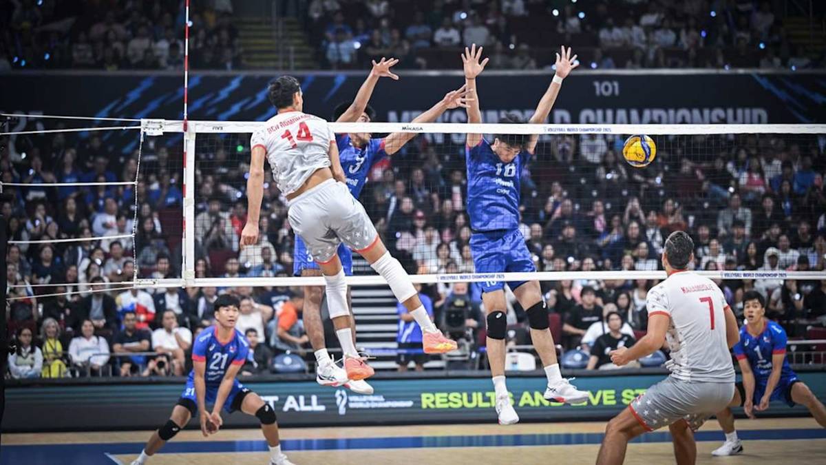 Gracze w siatkówkę podczas meczu, jeden z nich wyskakuje do zbicia piłki, podczas gdy inny blokuje.