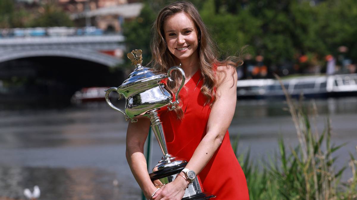 Kobieta w czerwonej sukience trzyma wielki, srebrny puchar.