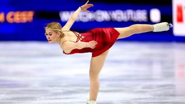 Łyżwiarka figurowa w czerwonej sukience wykonuje pozycję na lodzie.