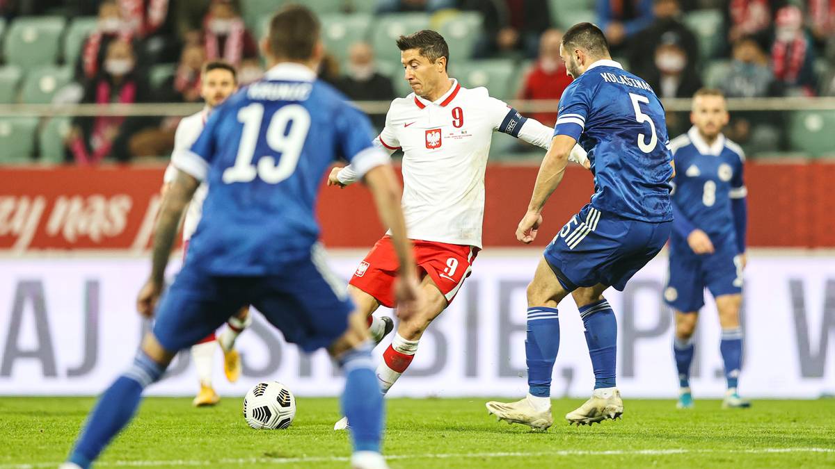 Piłkarze reprezentacji Polski w białych strojach walczą o piłkę z zawodnikami Bośni i Hercegowiny w niebieskich koszulkach.