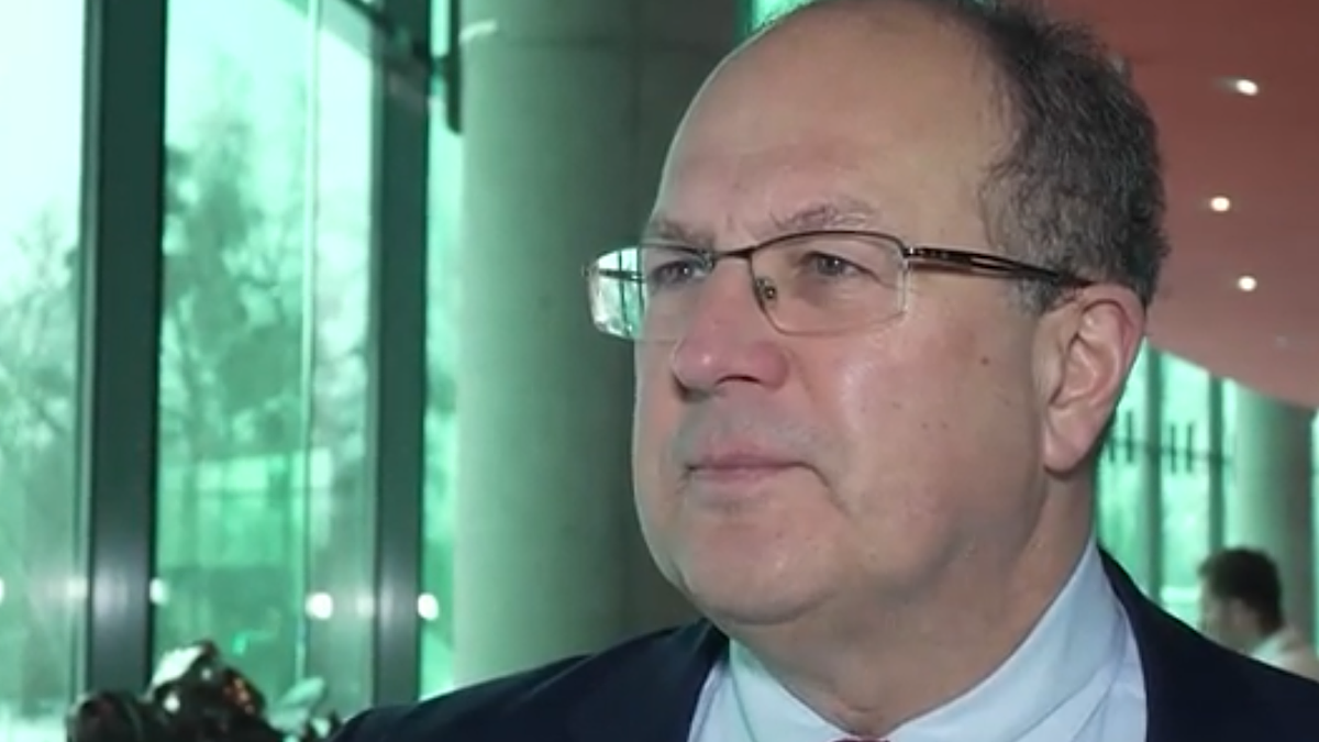 Mężczyzna w okularach i garniturze, mówiący do kamery.