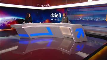 Dwie osoby siedzące przy stole w studiu telewizyjnym z ekranem w tle.