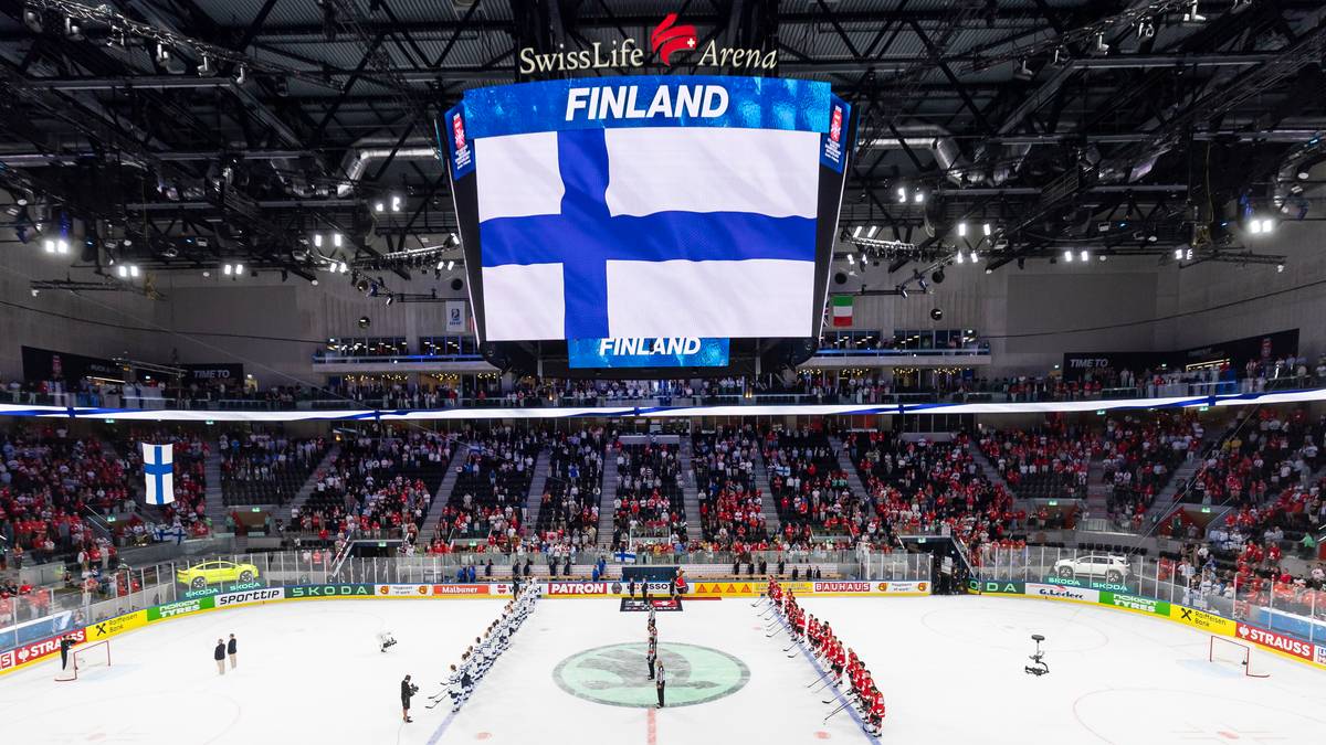 Widok na lodowisko podczas meczu hokeja na lodzie z flagą Finlandii na telebimie.