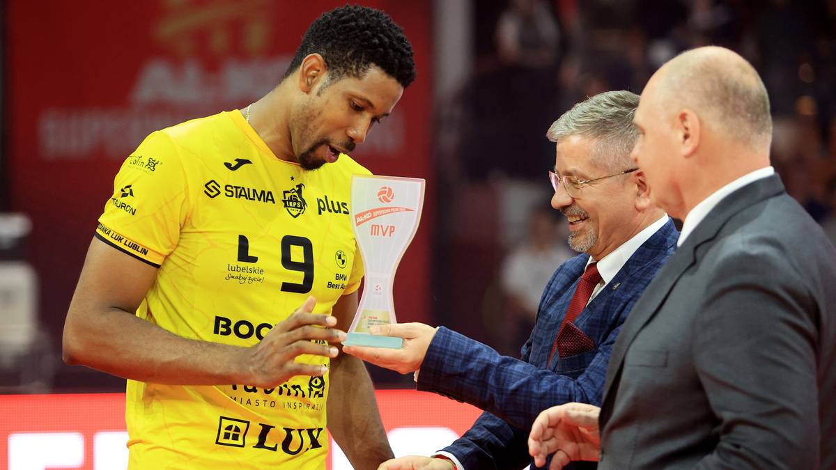 Siatkarz w ż&oacute;łtej koszulce z numerem 9 otrzymuje trofeum od mężczyzny w garniturze.