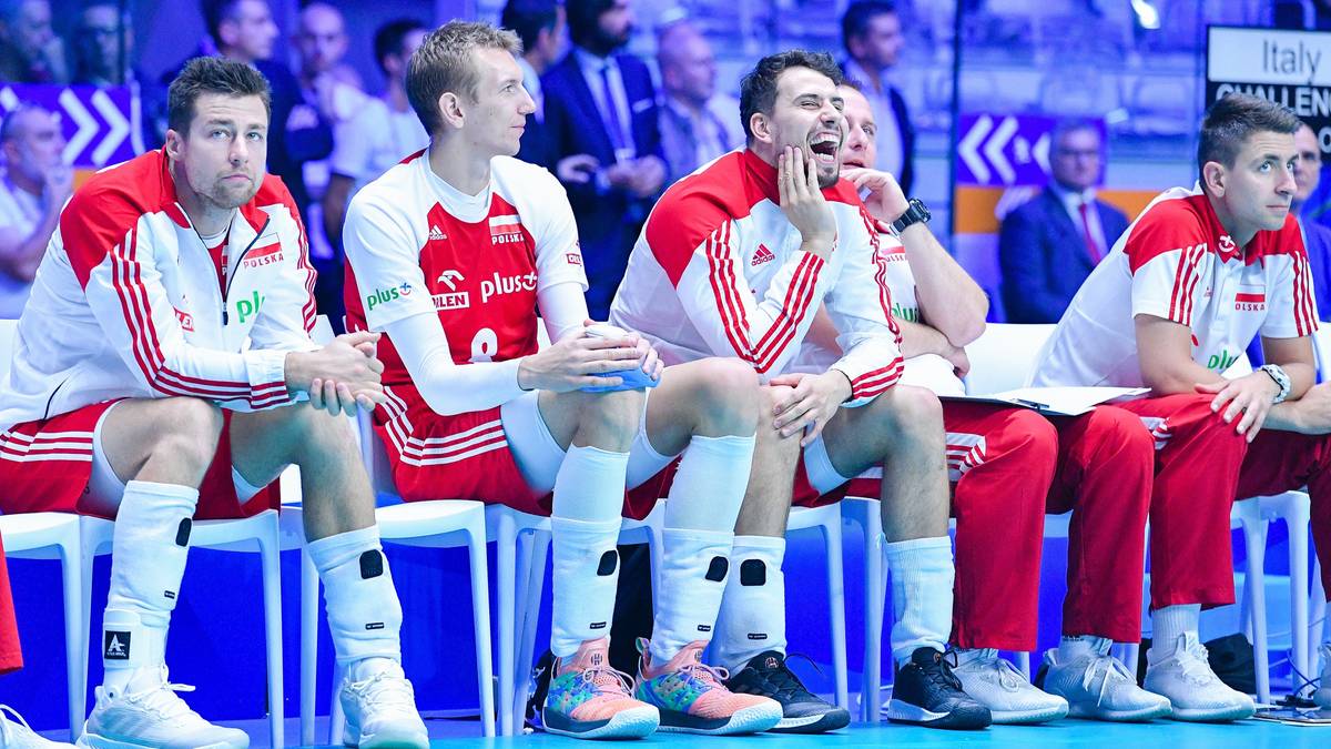 Siedmiu siatkarzy w czerwono-białych strojach reprezentacji Polski siedzi na ławce rezerwowych podczas meczu.