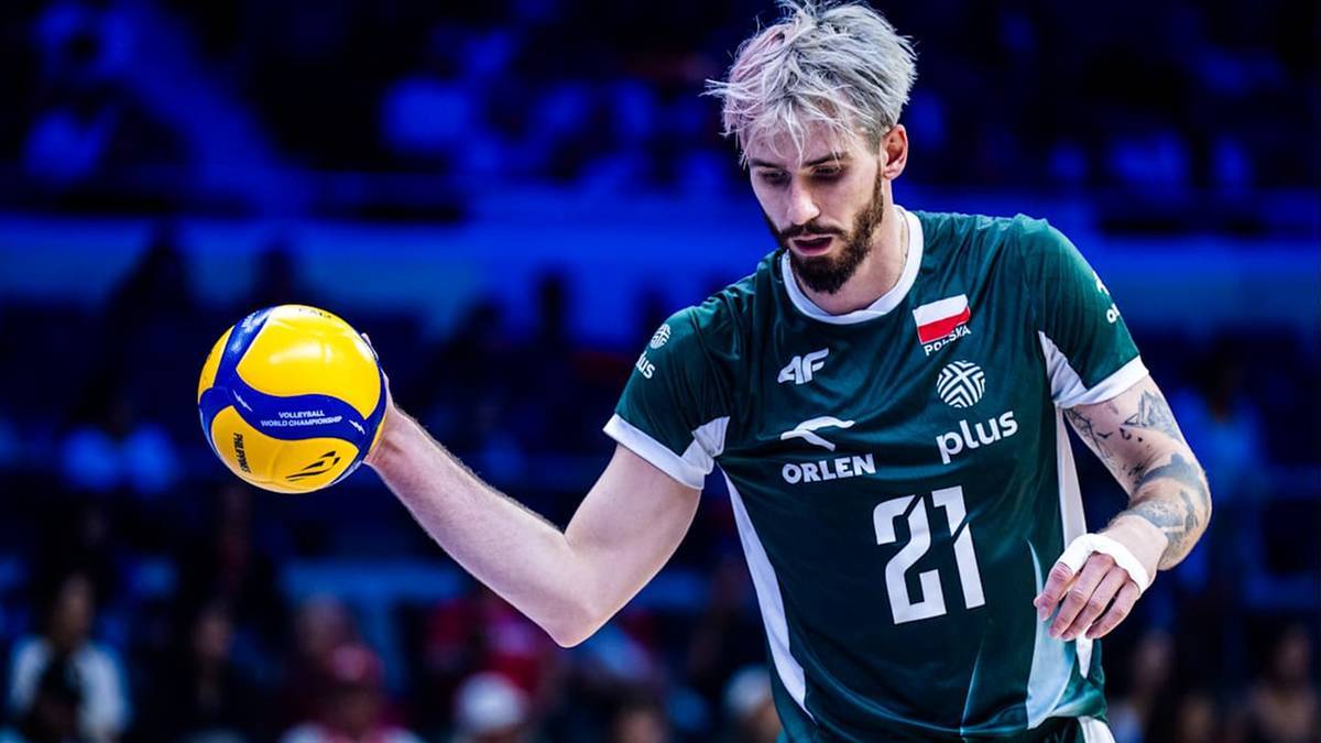 Siatkarz w zielonej koszulce z numerem 21 trzymający piłkę do siatk&oacute;wki.