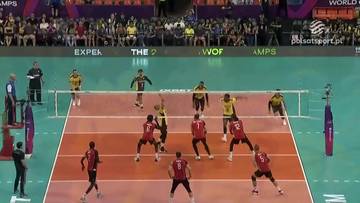 Siatkarze w akcji podczas meczu, jeden z zawodnik&oacute;w wykonuje zagrywkę, pozostali gracze są na boisku, gotowi do odbicia piłki.