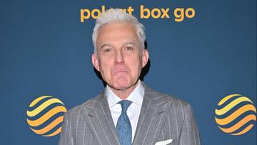 Mężczyzna w dwurzędowym, szarym garniturze w prążki, z jasnoniebieskim krawatem i białym poszetką.