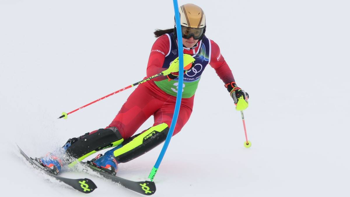 Narciarka alpejska w czerwonym stroju zjazdowym pokonuje zakręt na stoku narciarskim, używając kijk&oacute;w i nart.