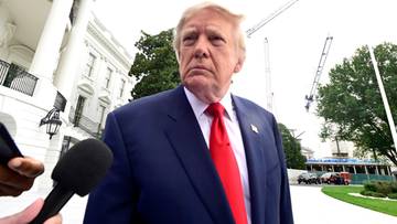 Donald Trump ubrany w granatowy garnitur i czerwoną krawat, stojący na tle Białego Domu podczas konferencji prasowej.