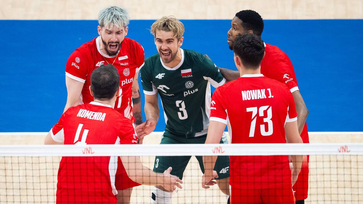 Pięciu polskich siatkarzy w strojach sportowych, dwóch w zielonych z numerami na plecach, trzech w czerwonych z numerami na plecach, wszyscy stoją w rzędzie z rękami na barkach swoich kolegów, patrząc w stronę przeciwnika.