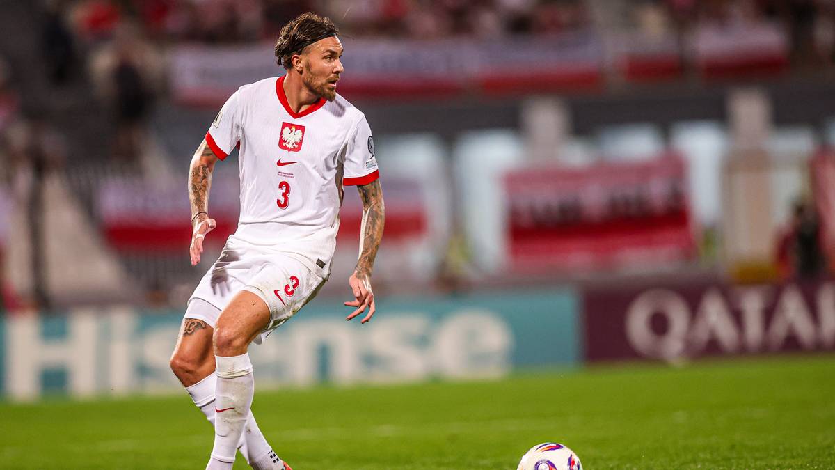 Piłkarz w białej koszulce z godłem Polski na piersi, z numerem 3 na plecach, biegnie po zielonej murawie stadionu w kierunku piłki.