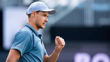 Kamil Majchrzak, polski tenisista, w czapce i koszulce sportowej, z zaciśniętą w pięść prawą ręką, na tle trybun.