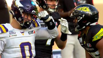 Dwóch zawodników futbolu amerykańskiego podczas meczu, jeden w białym stroju z fioletowymi i żółtymi pasami, drugi w czarnym stroju z żółtymi błyskawicami.