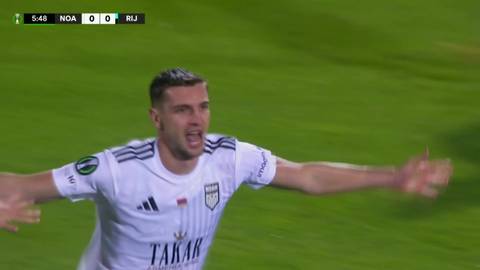 Piłkarz Nardin Mulahusejnović w białej koszulce z ciemnymi pasami na ramionach, radośnie świętuje zdobycie bramki. Jest w ruchu, z otwartymi ramionami i wykrzywionymi ustami, krzycząc. Na tle zielona murawa boiska piłkarskiego. W lewym g&oacute;rnym rogu ekranu widać wynik meczu 0:0.