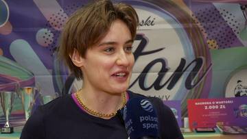 Katarzyna Zillmann, młoda kobieta o kr&oacute;tkich brązowych włosach, ubrana w ciemną bluzę z kolorowym kołnierzem i złotym łańcuszkiem, m&oacute;wi do mikrofonu z logo "Polsat Sport". W tle widoczne są puchary, baner z napisem "Stan" oraz tablice informacyjne.