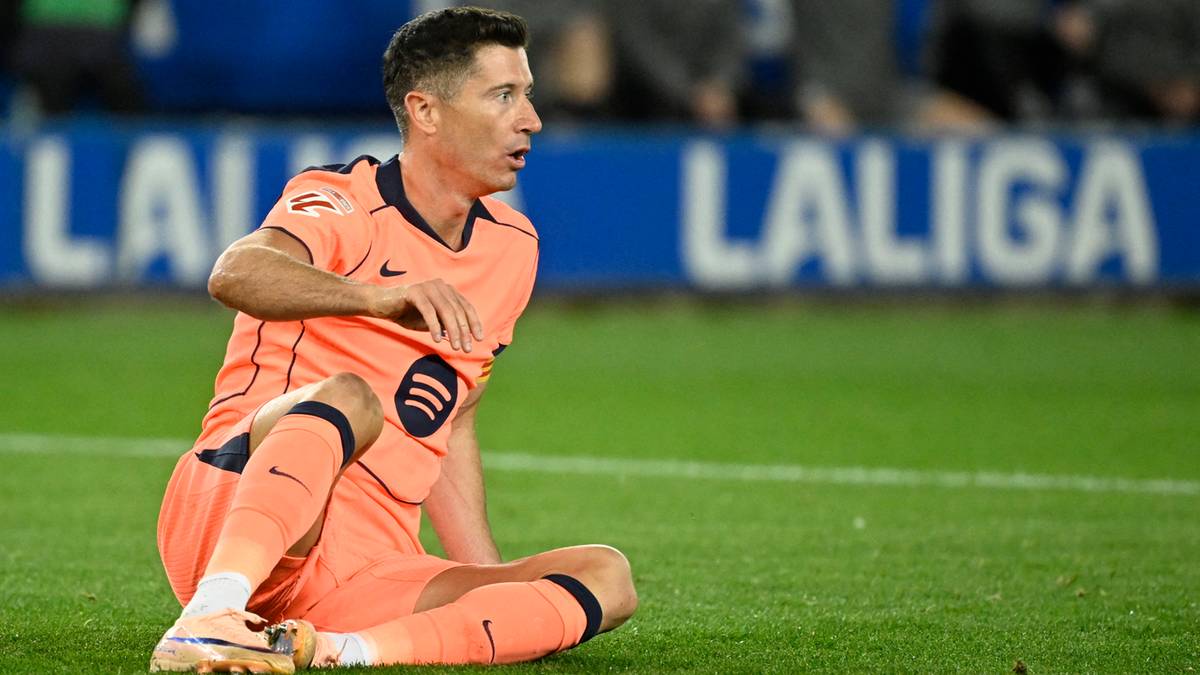 Robert Lewandowski siedzi na boisku piłkarskim w pomarańczowym stroju.