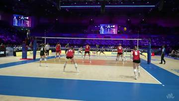 Mecz siatk&oacute;wki kobiet w hali sportowej, siatkarki przy siatce, trybuny z publicznością w tle.