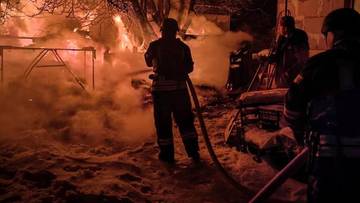 Strażacy gaszą nocny pożar, widoczny dym i płomienie.